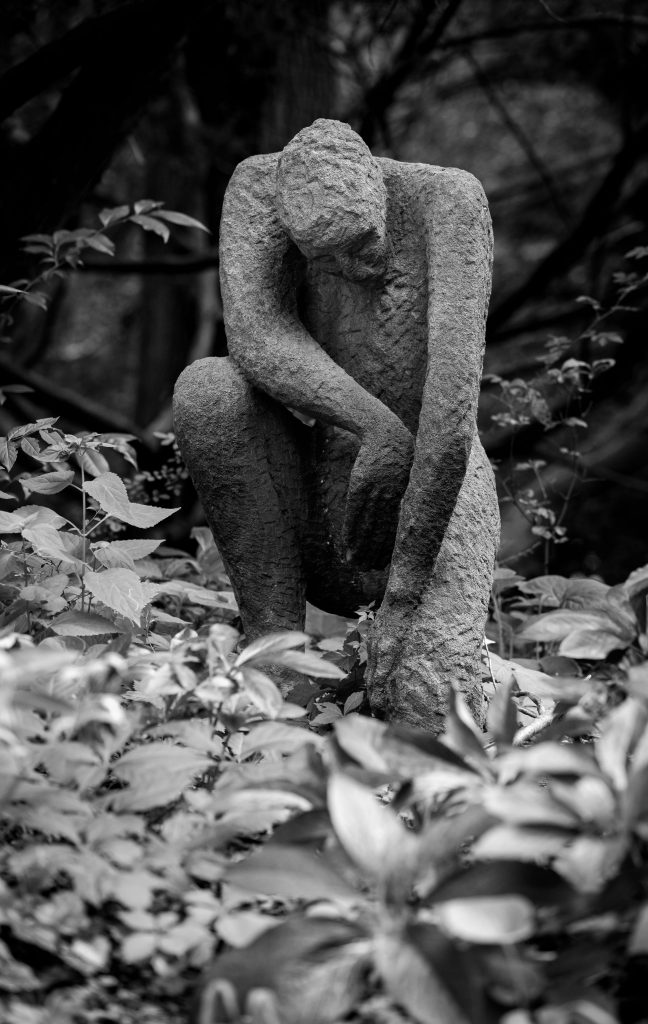 Black and white image of a stone sculpture surrounded by lush foliage, exuding a tranquil and contemplative atmosphere. Kontemplative Atmosphäre als Sinnbild der philosophischen Bewusstseinsanalyse